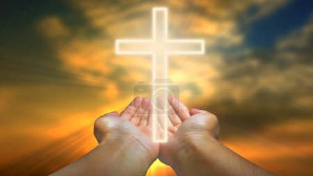 Hands holding christian cross against blue sky with white clouds and sun