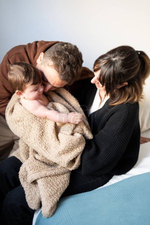 parents laughing with baby in room, eight-month-old baby with brown blanket, first-time parents playing with newborn baby