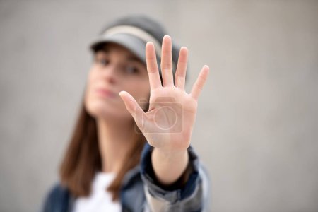 Foto de Hand saying stop in foreground, in background out of focus girl in cap with serious face - Imagen libre de derechos