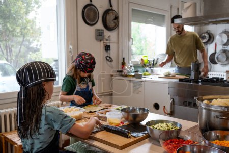 Vater kocht und seine beiden Töchter in Schürzen und Hüten bereiten in der Küche Sushi zu, rollen den Reis zusammen und legen ihn mit vegetarischen Makis aus. Familie in der Küche lernt