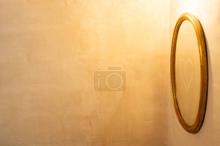 Mirror with golden frame with tarnished glass, drawn a heart, horizontal photograph with a lot of copyspace of fine cream cement texture