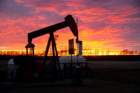 Striking orange and purple sunrise in prairies and the silhouette of an oil pump extracting fuel.