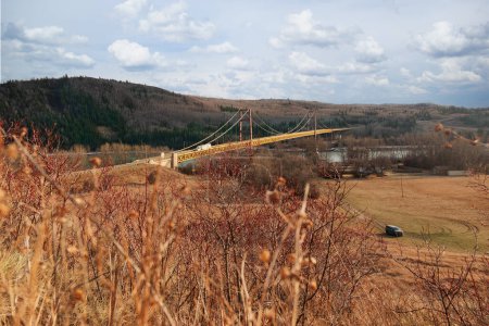 Scenic spring view of a yellow iron bridge with trusses over the river, hills with with forest around. Dunvegan bridge, Alberta, Canada.