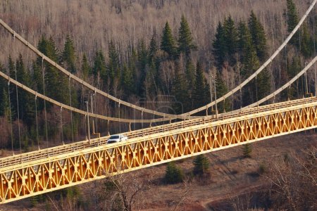 Scenic spring view of a car on a yellow iron bridge with trusses over the river, woodland with spruce around. Dunvegan bridge, Alberta, Canada.