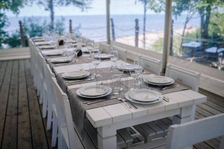 Téléchargez les photos : Une table couverte de blanc pour un événement sous un auvent blanc sur le bord de la mer - en image libre de droit