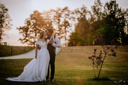 Téléchargez les photos : Les jeunes mariés se regardent et s'embrassent en amour au coucher du soleil - en image libre de droit