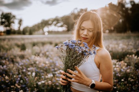 Photo for A young woman in a white shirt with rye flowers in her hands in a field of rye flowers - Royalty Free Image