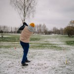 A man makes a shot with a club on the golf course in winter