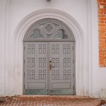 The grey church door, set against the backdrop of a sturdy brick entrance, exudes a sense of timeless elegance and welcomes worshippers with a touch of solemn beauty.