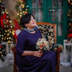 A senior woman in a purple dress sits among Christmas decorations