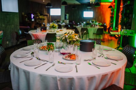 mesa redonda elegantemente establecida para un evento gastronómico. La mesa está cubierta con un mantel blanco crujiente y se establece con placas, cubiertos y cristalería para cada ajuste de lugar..