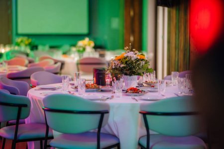 Foto de Primer plano de una mesa de comedor para un banquete o un evento formal, con cristalería, platos de cerámica y un arreglo floral central. - Imagen libre de derechos