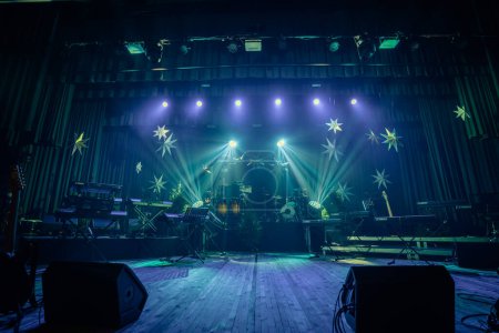 Téléchargez les photos : Valmiera, Lettonie - 28 décembre 2023 - scène de concert avec divers instruments de musique, y compris des claviers, des tambours et des guitares, prêts pour une performance. La scène est éclairée par un éclairage dramatique - en image libre de droit