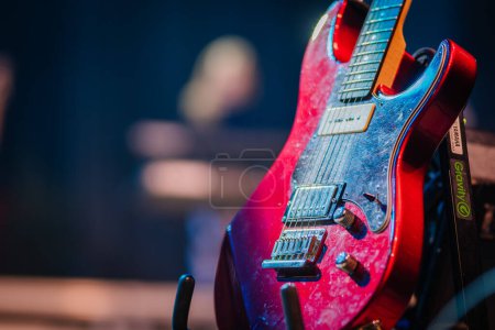 Photo for Valmiera, Latvia - December 28, 2023 - Close-up of a red electric guitar with a glossy finish resting on a stand with stage lights reflecting on its surface and a blurred background. - Royalty Free Image
