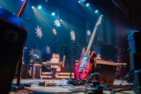 Téléchargez les photos : Valmiera, Lettonie - 28 décembre 2023 - guitare électrique rouge sur un stand, mise en scène avec projecteurs et effets de scène en arrière-plan. - en image libre de droit