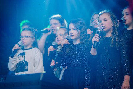 Téléchargez les photos : Valmiera, Lettonie - 28 décembre 2023 - groupe de jeunes filles chantant dans des microphones sur une scène avec un éclairage bleu et un effet de fumée en arrière-plan. - en image libre de droit