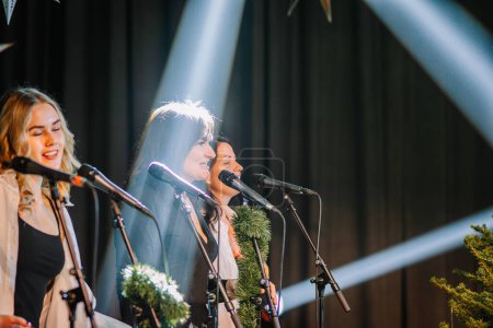Téléchargez les photos : Valmiera, Lettonie - 28 décembre 2023 - trois femmes chantent dans des microphones, avec des lumières de scène qui les illuminent d'en haut. - en image libre de droit