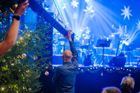 Photo for Valmiera, Latvia - December 28, 2023 - person adjusting stage equipment, with Christmas trees, lights, and a stage with musical instruments in the background - Royalty Free Image