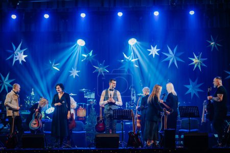 Valmiera, Lettland - 28. Dezember 2023 - Band auf der Bühne mit verschiedenen Musikern und Instrumenten, beleuchtet durch blaues Licht und sternförmige Dekorationen.