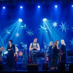 Valmiera, Latvia - December 28, 2023 - band on stage with various musicians and instruments, illuminated by blue lights and star-shaped decorations.