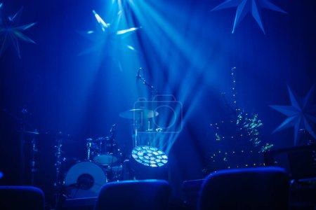 Bühne mit Schlagzeug und Weihnachtsbaum, beide unterstrichen durch dramatische blaue Bühnenlichter und Sternenformen im Hintergrund