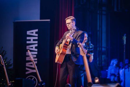 Téléchargez les photos : Valmiera, Lettonie - 28 décembre 2023 - homme jouant de la guitare sur une scène avec Yamaha signalisation, un autre musicien en arrière-plan, et l'éclairage de la scène. - en image libre de droit