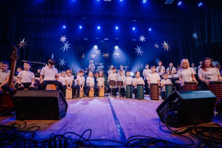 Téléchargez les photos : Valmiera, Lettonie - 28 décembre 2023 - groupe d'enfants sur scène jouant avec des tambours de cajon, un guitariste et un batteur. La scène est décorée d'étoiles. - en image libre de droit