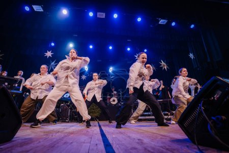 Foto de Valmiera, Letonia - 28 de diciembre de 2023 - niños con atuendos blancos interpretan enérgicamente una rutina de baile en el escenario con decoraciones de estrellas y luces de escenario azules - Imagen libre de derechos
