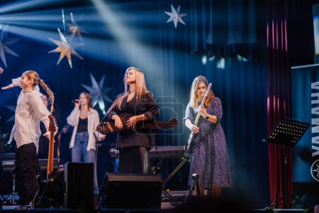 Foto de Valmiera, Letonia - 28 de diciembre de 2023 - músicos en el escenario con instrumentos, una cantante y decoraciones estrella bajo iluminación azul. - Imagen libre de derechos