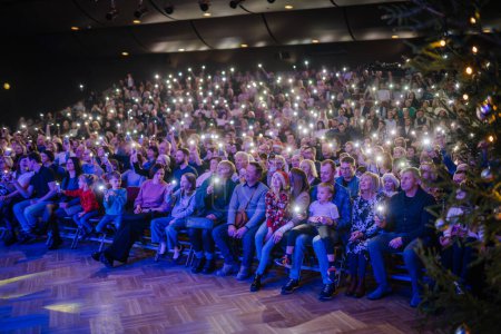 Téléchargez les photos : Valmiera, Lettonie - 28 décembre 2023 - grand public avec des lumières de leurs téléphones créant un effet scintillant, avec un arbre de Noël au premier plan - en image libre de droit