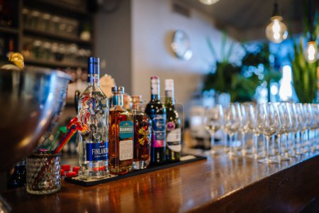 Foto de Riga, Letonia - 6 de diciembre de 2023 - selección de bebidas alcohólicas en un mostrador de bar con una fila de copas de vino limpias en el fondo, creando un ambiente acogedor para socializar. - Imagen libre de derechos
