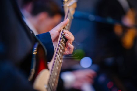 Photo for Riga, Latvia - December 6, 2023 - hands of a musician playing an electric bass guitar with a blurred background, focusing on the strings and fretboard. - Royalty Free Image