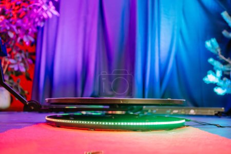 360-degree photo booth platform on a red carpet with a colorful backdrop, including a blue curtain and a plant.