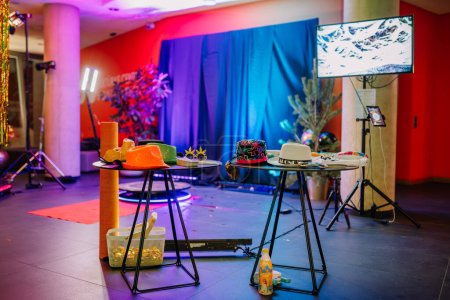 Sigulda, Lettonie - 12 janvier 2023 - installation de fête avec deux tables affichant des chapeaux et accessoires colorés, un moniteur, une toupie de cabine photo à 360 degrés, un éclairage festif et un rideau de scène bleu.