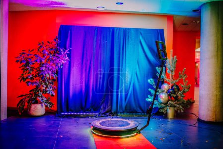 indoor photography setup with a 360-degree spinner, colorful lighting, a stage curtain backdrop, festive decorations. Defocused view of a 360 photo booth