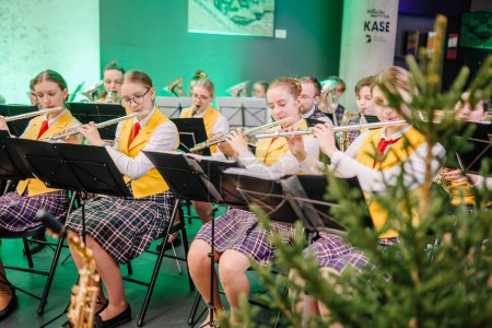 Photo for Sigulda, Latvia - January 12, 2023 - group of focused young musicians playing flutes in an orchestra, wearing yellow vests and plaid skirts in an indoor venue with greenery in the foreground. - Royalty Free Image
