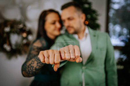 Foto de Pareja recién comprometida tomados de la mano para mostrar sus anillos, con un árbol de Navidad borroso en el fondo. - Imagen libre de derechos