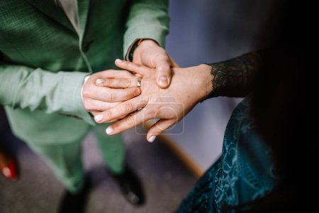 Foto de Un primer plano de un par de manos, con anillos de boda, la mujer en manga de encaje y el hombre en un traje verde. - Imagen libre de derechos