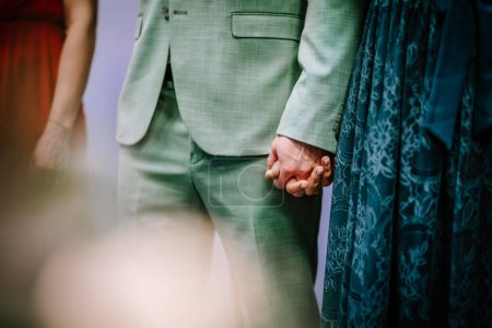 Photo for A close-up of a couple holding hands, the man in a green suit and the woman in a blue lace dress. - Royalty Free Image