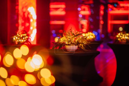 Foto de Primer plano de un centro de mesa festivo con luces y fondo bokeh borroso en un espacio para eventos de tonos rojos. - Imagen libre de derechos