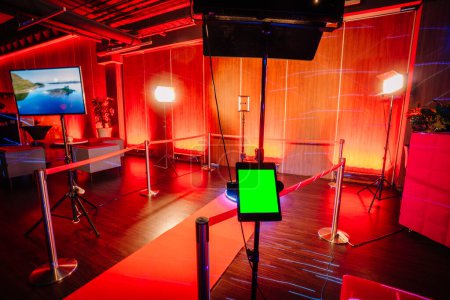 Foto de Configuración de la cabina de fotos del spinner 360 con una alfombra roja, equipo de iluminación y una pantalla en un espacio para eventos iluminado por el rojo. - Imagen libre de derechos