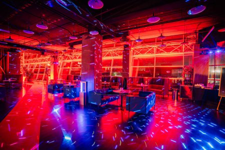 indoor lounge with modern furniture bathed in vibrant red and blue lights, reflecting off the floor and ceiling.