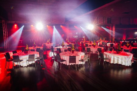 banquet hall with tables set for a festive event, illuminated by striking stage lights and spotlights.