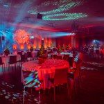 banquet hall with festive tables, a lit Christmas tree centerpiece, and a striking light display with blue and red lights.