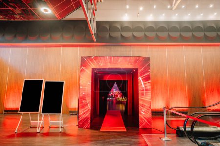 entrance with dynamic red lighting effects leading to an event space, flanked by blank signage boards