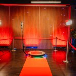 360 spinner photo booth setup in an event space with ambient red lighting, red carpet, lounge furniture, and dynamic blue laser lights.