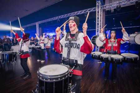 Photo for Riga, Latvia - December 18, 2023 -  group of drummers in Latvian hockey jerseys, energetically playing drums with blue stage lights in the background. - Royalty Free Image