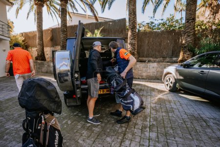 Téléchargez les photos : Malaga, Espagne - 21 janvier 2024 - personnes chargeant des sacs de golf à l'arrière d'un VUS dans une allée entourée de palmiers. - en image libre de droit