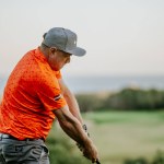 Malaga, Spain - January, 21, 2024 - A close-up of a man in mid-golf swing, wearing an orange shirt, gray pants, and a gray cap, with a blurred background.
