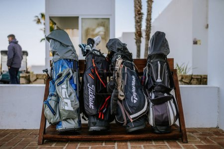 Téléchargez les photos : Sotogrande, Espagne - 23 janvier 2024 - gamme de sacs de golf sur un banc, avec un homme en arrière-plan dans un complexe de golf. - en image libre de droit